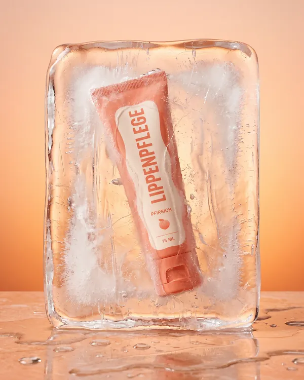 KI-generiertes Produktbild: Lippenpflege in einem Eisblock vor Pfirsichton